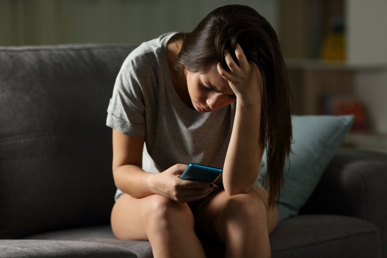 Triste adolescente víctima de acoso cibernético sentado en un sofá de la sala de estar en casa